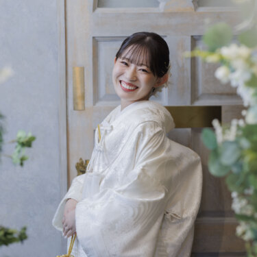 花の手まりブーケを持ち、振り返って満面の笑みを見せる白無垢の花嫁。和装スタジオフォトの花嫁ポートレート