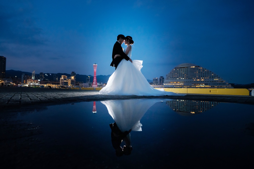 夕暮れの神戸ポートタワーを背に、水たまりのリフレクションに映るおでこ合わせの新郎新婦の幻想的なフォトウェディング