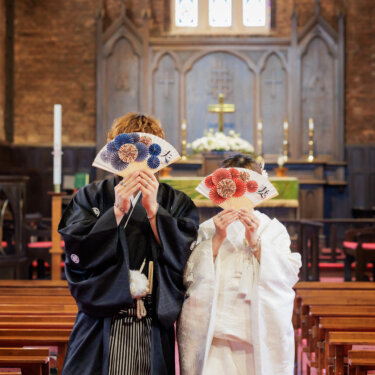 祭壇の前で扇子を広げて顔を隠す黒紋付袴の新郎と白無垢の花嫁。川口基督教会で撮る遊び心あるチャペル和装フォトウェディング