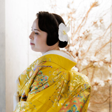 白い花の髪飾りをつけ、黄色の色打掛で横顔を見せる花嫁。衣装の金の刺しゅうが映える和装スタジオフォト