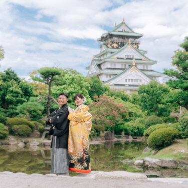 松と池の日本庭園の奥にそびえる大阪城天守閣を入れて、寄り添う新郎新婦を遠景で写した和装の結婚写真