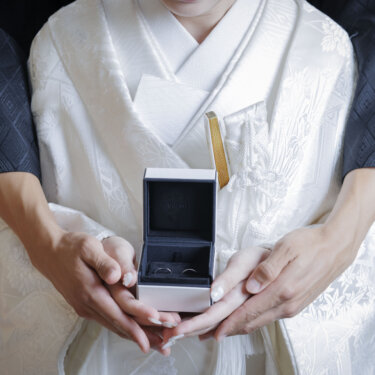 白無垢の花嫁の手に開いたリングボックスを、新郎が後ろから包み込むように支える手元の和装前撮りカット