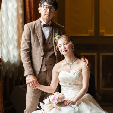 中央公会堂の特別室で、椅子に座る花嫁の手を取り肩を抱くタキシードの新郎。クラシカルな洋館で撮るフォトウェディング