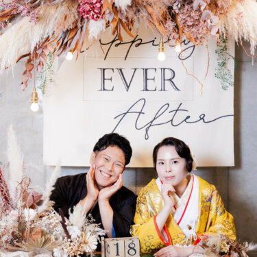 ドライフラワーで飾った'EVER After'の壁の前で、頬づえをついてほほえむ紋付袴の新郎と色打掛の花嫁。大人の和装スタジオフォト