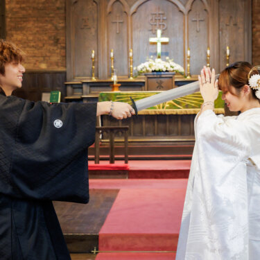 番傘を刀に見立てて受け止める白無垢の花嫁と紋付袴の新郎。教会の祭壇前で撮るユニークな和装チャペルフォトのアイデアショット