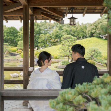 回廊のベンチから池と芝生の築山を眺める、白無垢の花嫁と紋付の新郎の後ろ姿。和装前撮りの人気ポーズ