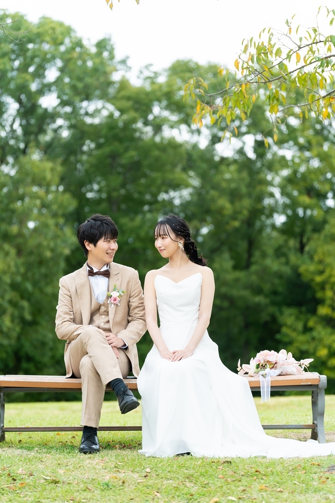 万博記念公園の芝生にドレスを広げて座り、肩を寄せ合って笑い合う新郎新婦