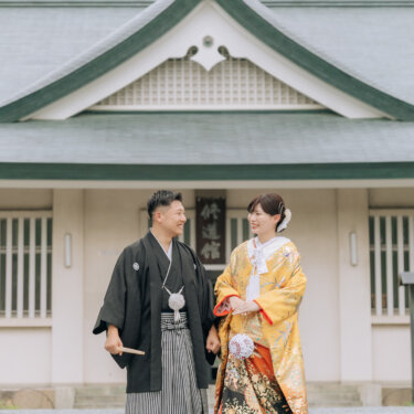 緑の屋根の和風建築の前に並んで立つ、紋付袴の新郎と色打掛の花嫁。大阪城公園内で撮る和装の結婚写真