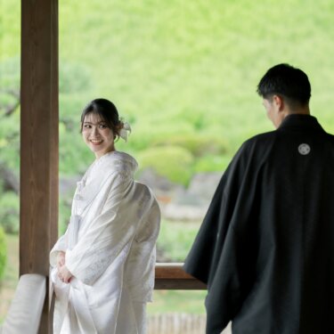 回廊の柱のそばで振り返って笑う白無垢の花嫁と、背を向けて歩く紋付の新郎。大仙公園で撮る和装ロケーションフォト
