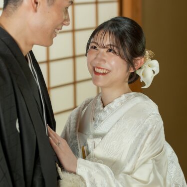 新郎の胸に手を添えて見上げ、満面の笑みを見せる白無垢の花嫁。和室で撮る仲睦まじい和装前撮りのポーズ