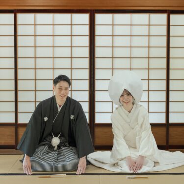 障子の前の畳で三つ指をついて並ぶ紋付袴の新郎と綿帽子の白無垢の花嫁。正座でごあいさつする和装前撮り
