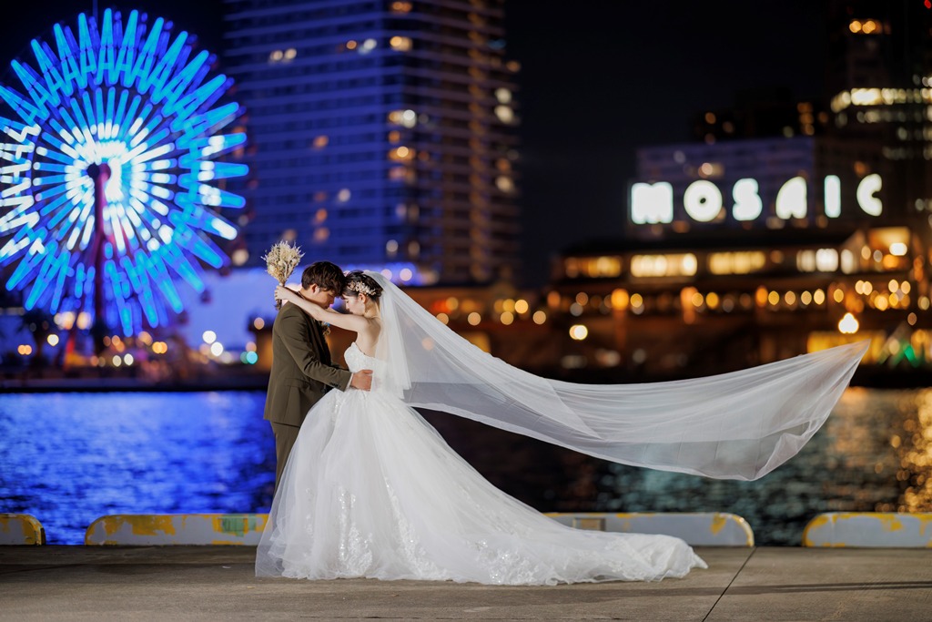 夜のハーバーランドの大観覧車のイルミネーションを背に、ロングベールをなびかせて抱き合う新郎新婦のナイトフォトウェディング