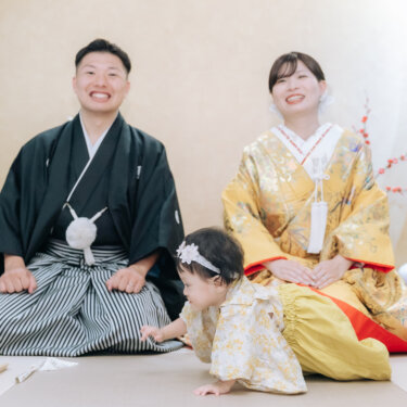 正座する新郎と色打掛の花嫁の前を、髪飾りを付けた赤ちゃんがはいはいする家族写真。お子様と叶える和装前撮り