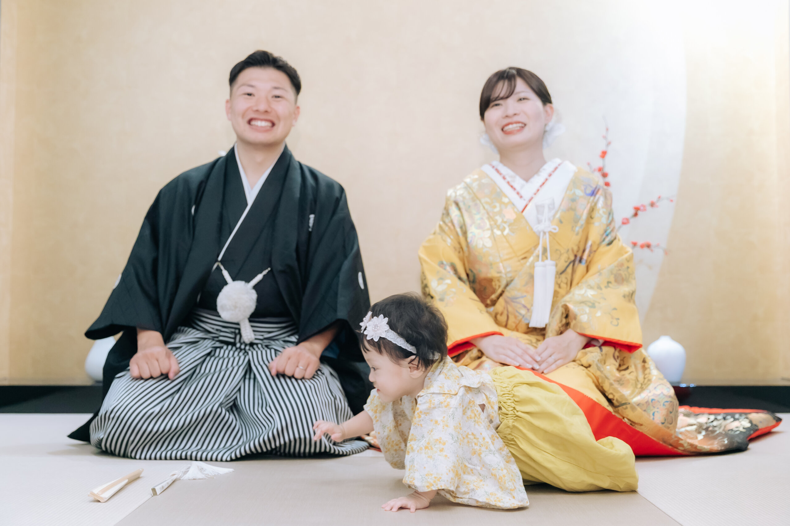 黄色の色打掛の花嫁様と羽織袴の花婿様の前を、和装姿の赤ちゃんがハイハイして進んでいく和室の写真