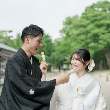新郎が差し出すお団子を笑顔で食べようとする白無垢の花嫁。食べ歩き風の小物が楽しい和装前撮りのワンシーン