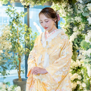 白い花とグリーンのフラワーアーチを背に、伏し目がちにたたずむ黄色の色打掛の花嫁の和装前撮り