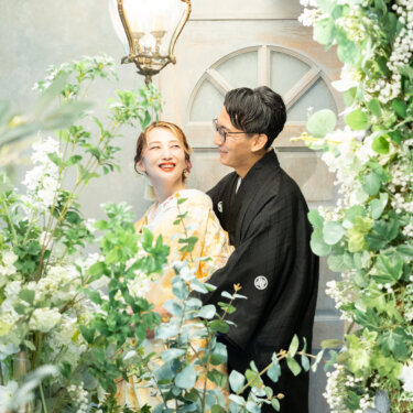 シャンデリアとグリーンに囲まれたスタジオで、色打掛の花嫁を後ろからそっと抱き寄せる紋付袴の新郎の結婚写真