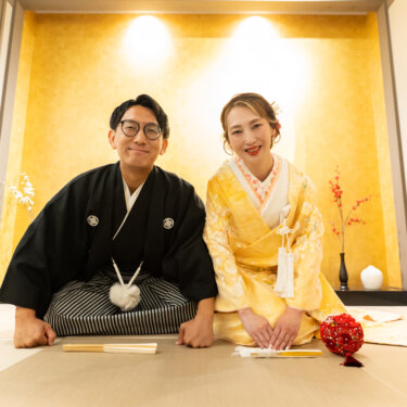 畳の和室スタジオでかしこまって座り、にっこり笑う紋付袴の新郎と色打掛の花嫁の結婚写真