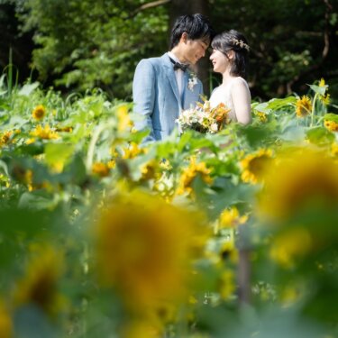 布引ハーブ園のひまわり畑で、ブルーのジャケットの新郎とウェディングドレスの花嫁が見つめ合う洋装の前撮り
