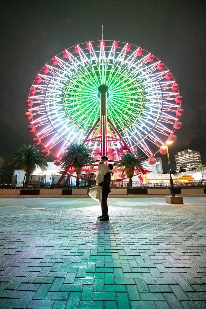色とりどりにライトアップされたハーバーランドの大観覧車の前で、向かい合って手を取る新郎新婦のナイトフォト前撮り