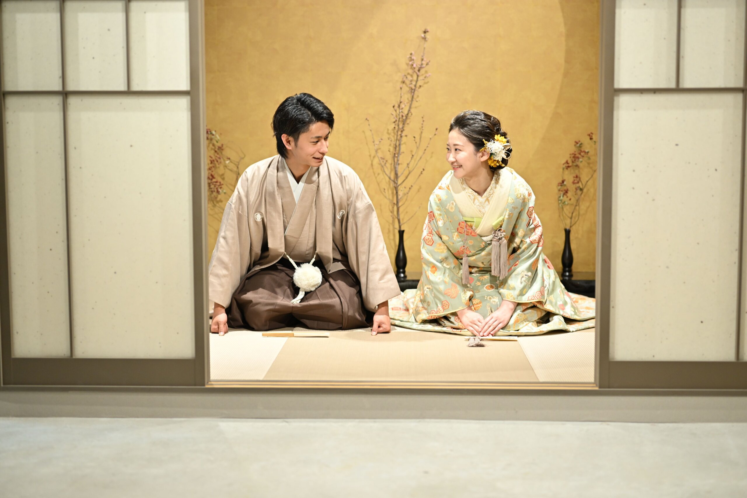 心斎橋店のスタジオ茶室で、丸窓のやわらかな光を背に寄り添う色打掛の花嫁と紋付袴の新郎