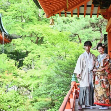 京都の毘沙門堂の朱色の回廊で、紋付袴の新郎と色打掛の花嫁が新緑を背に並ぶ和装の前撮り